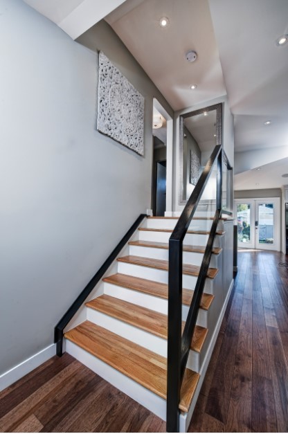 Modern staircase design with light wood treads, white risers, and black trim/railings. The guard rail is clear glass enclosed in black trim.