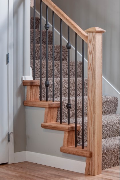 Carpeted staircase with wrought iron balusters and wood railing/posts.