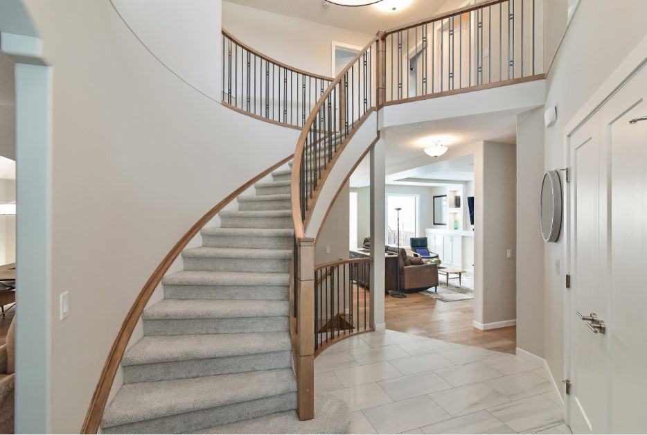 Renovated curved staircase with carpeted stairs, wood trim that matches the hardwood flooring in the living room, and wrought iron balusters for an open look